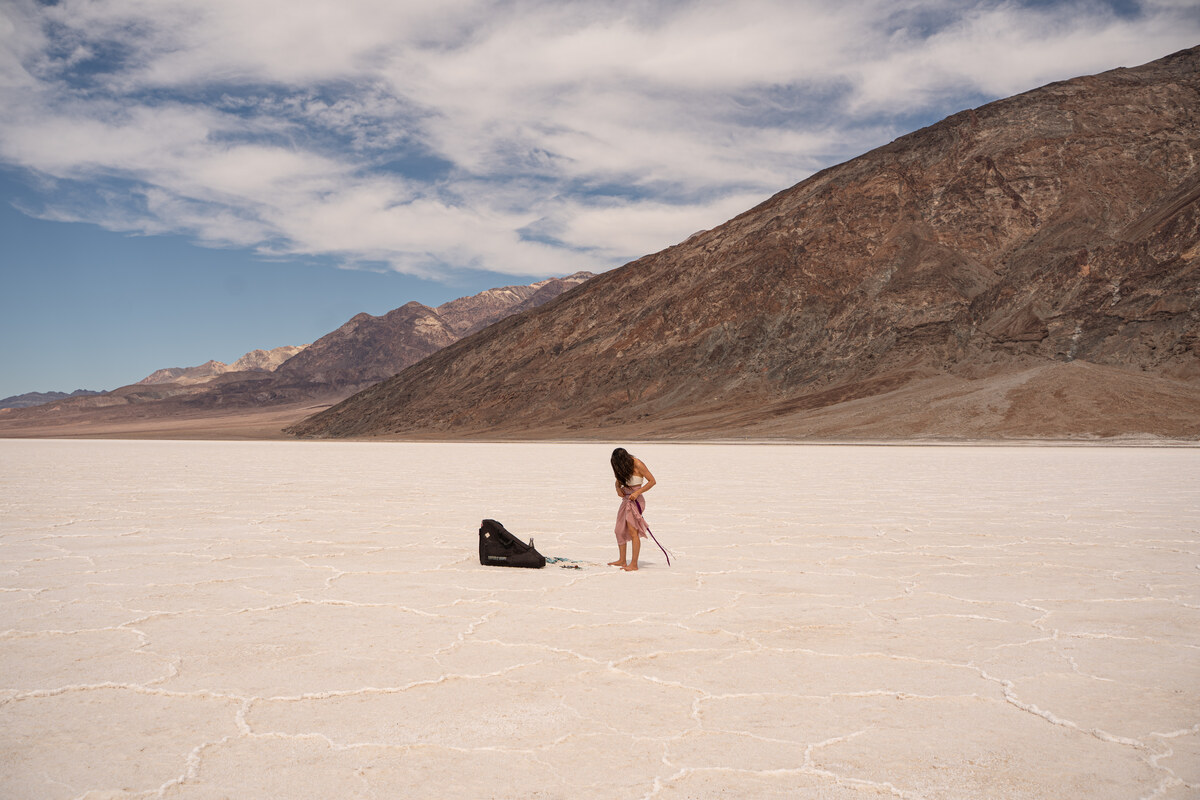 Melissa standing beside a dark bag on the salt flats below a broad mountain slope.
