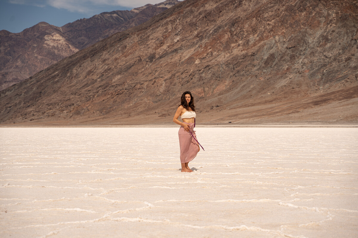 Melissa facing the camera in an ivory top and dusty rose wrap, with salt flats and a rocky mountain behind her.