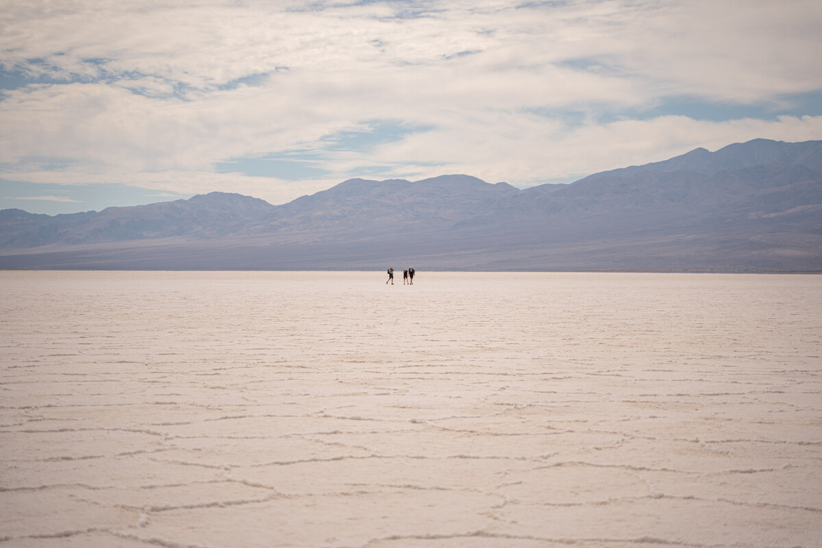 Tiny distant visitors on a broad salt flat beneath blue-gray mountains and a cloud-filled sky.